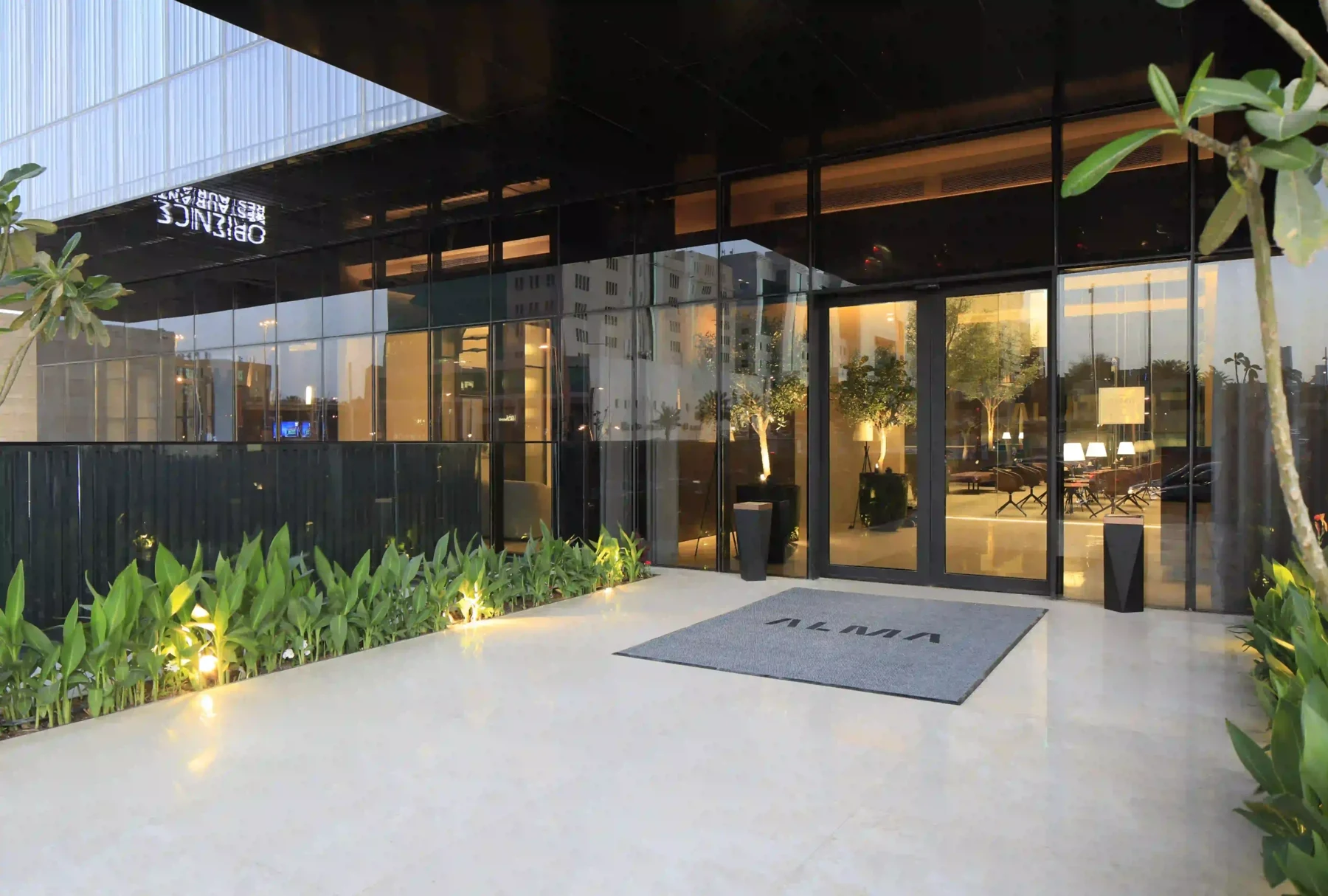 Alma hotel entrance with glass doors and landscaped planting